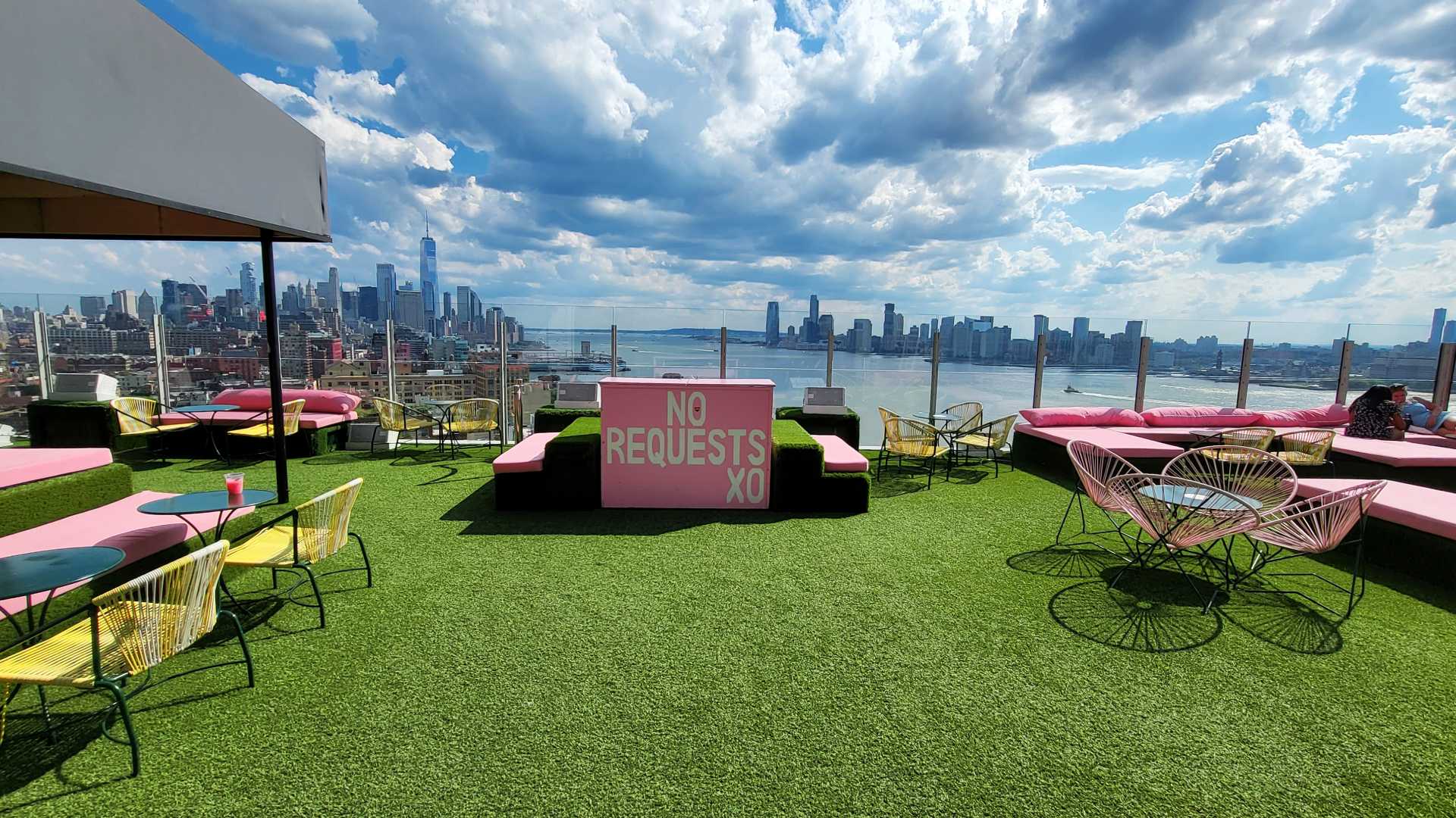 Pink no requests sign at DJ booth on artificial grass rooftop bar